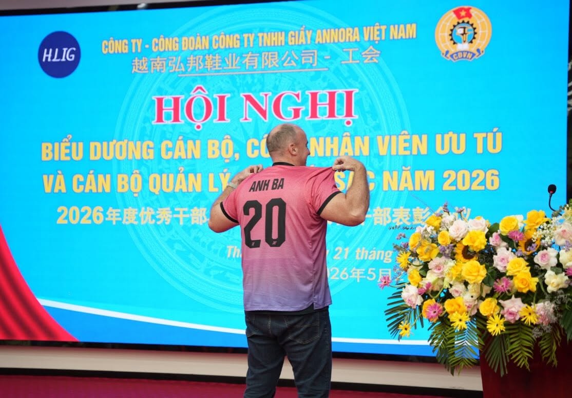 Derek on stage at an Annora Vietnam staff recognition event wearing a jersey reading Anh Ba 20